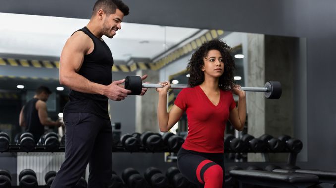 Personal instructor helping woman barbell squats